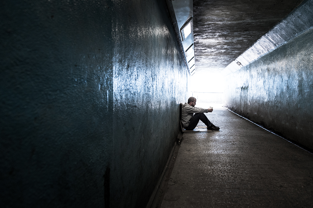 Young homeless adult male sitting and begging in subway tunnel